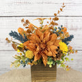 Cozy Harvest fall arrangement with orange and yellow flowers, blue accents and pinecones in a rustic wooden cube