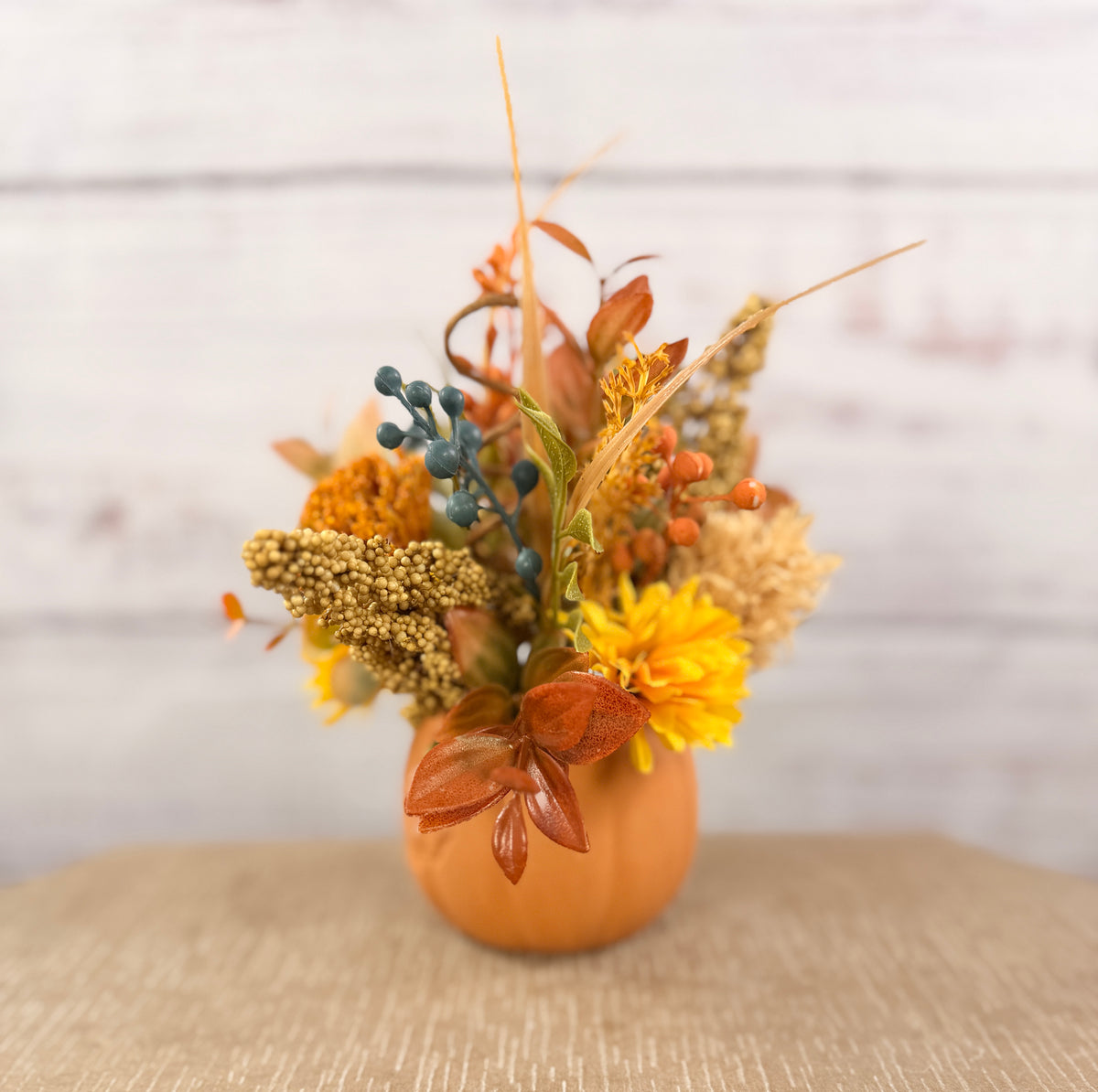 Harvest Grin smiling pumpkin with yellow and orange faux fall flowers, berries and autumn leaves
