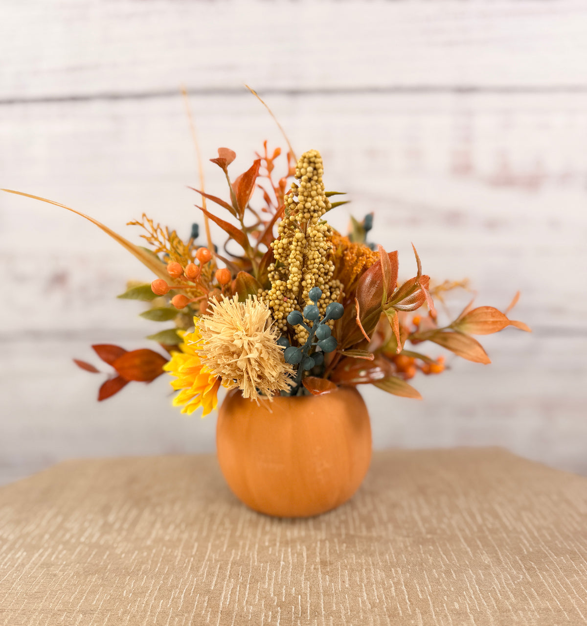 Harvest Grin smiling pumpkin with yellow and orange faux fall flowers, berries and autumn leaves