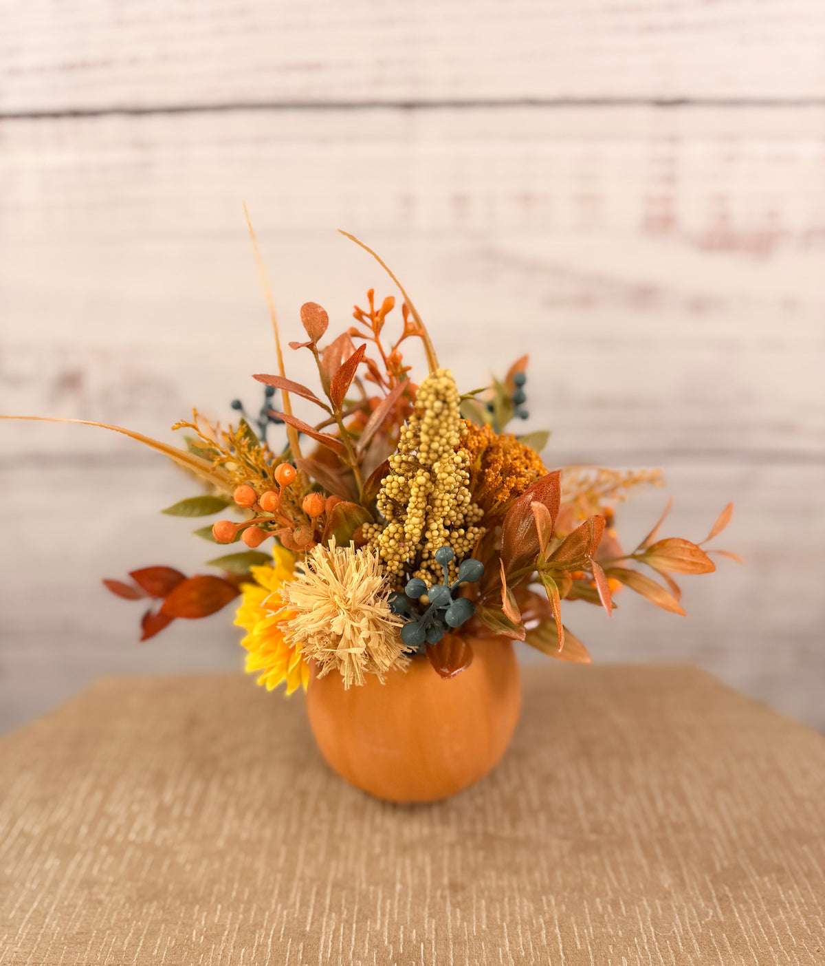 Harvest Grin smiling pumpkin with yellow and orange faux fall flowers, berries and autumn leaves