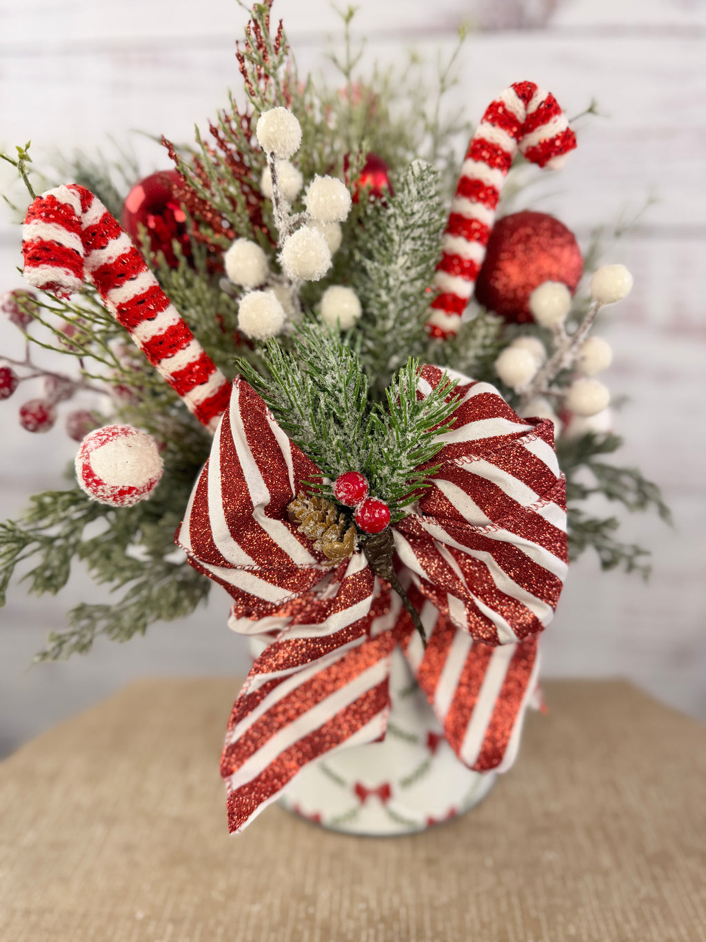 Handmade peppermint Christmas arrangement, white wall detail view of candy canes, striped bow and snowy greenery