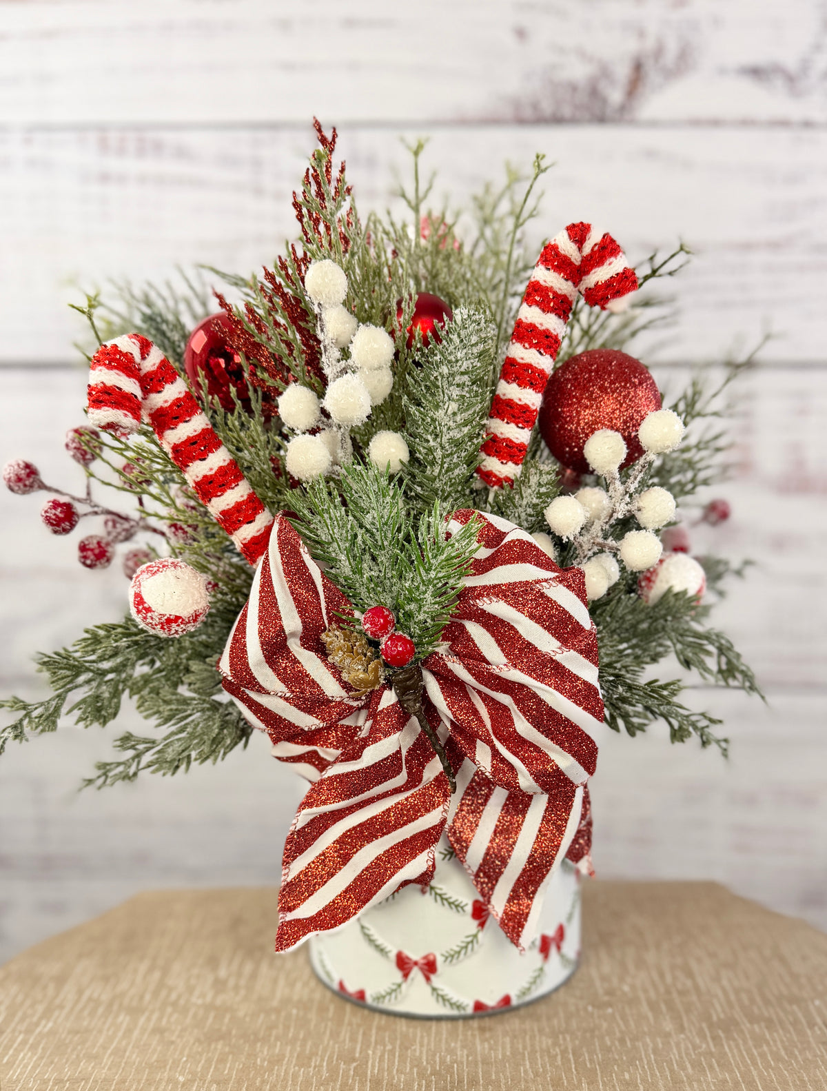 Handmade peppermint Christmas arrangement, white wall detail view of candy canes, striped bow and snowy greenery