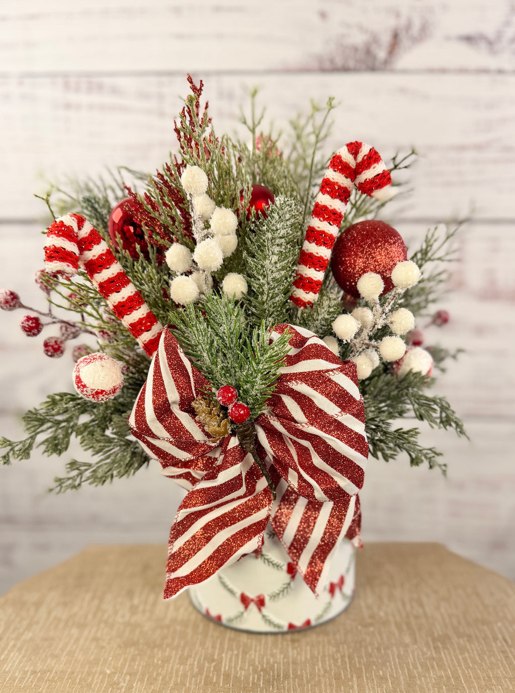 Handmade peppermint Christmas arrangement, white wall detail view of candy canes, striped bow and snowy greenery