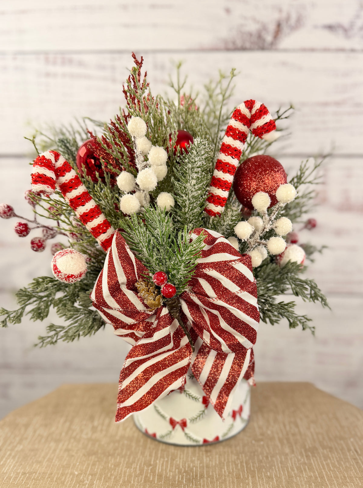 Handmade peppermint Christmas arrangement, white wall detail view of candy canes, striped bow and snowy greenery