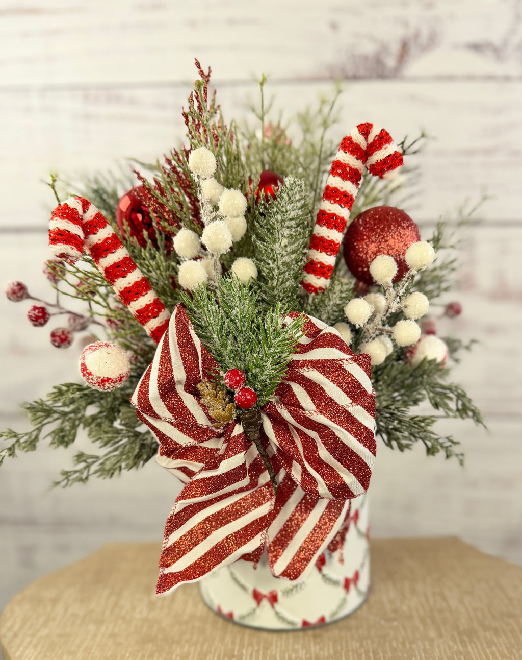 Handmade peppermint Christmas arrangement, white wall detail view of candy canes, striped bow and snowy greenery