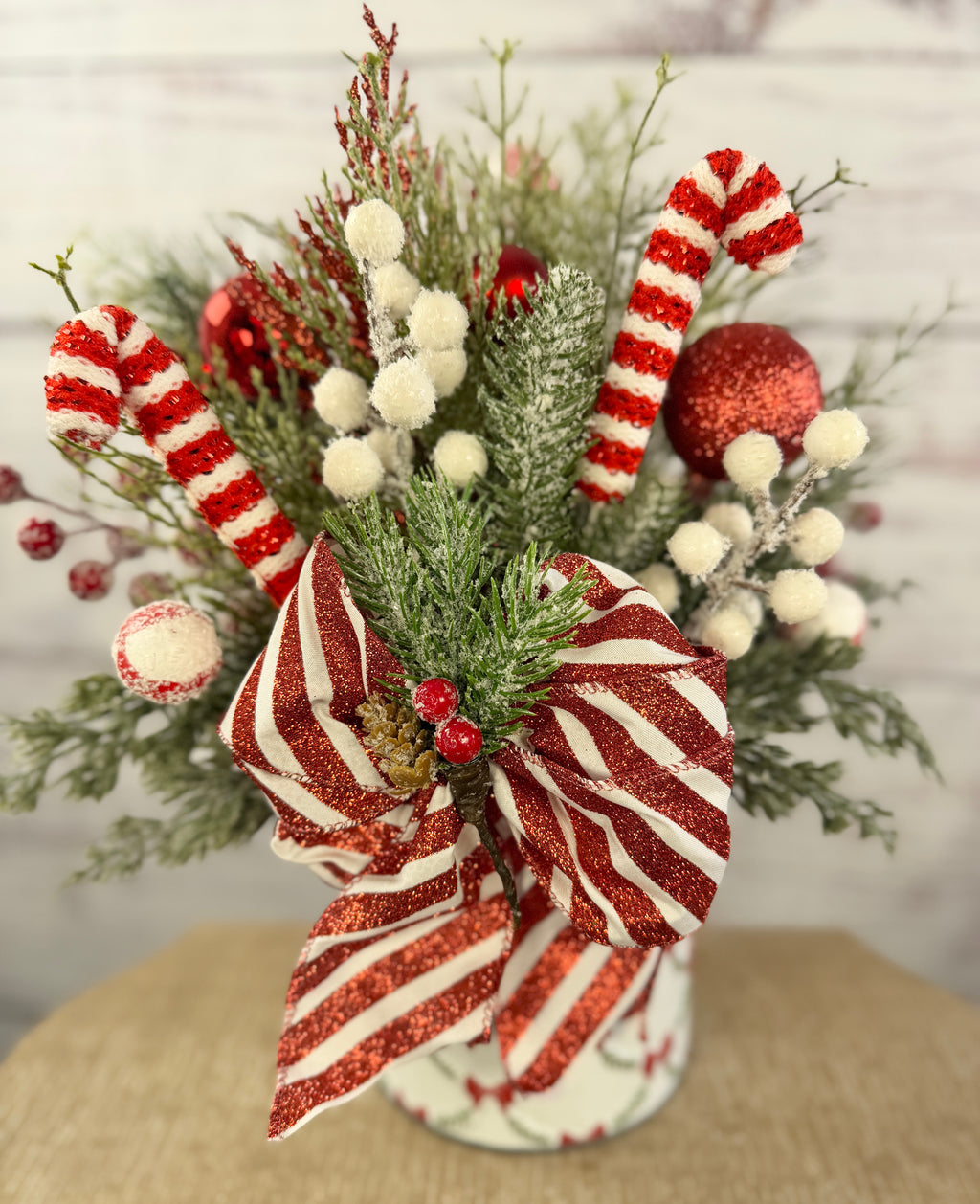 Handmade peppermint Christmas arrangement, white wall detail view of candy canes, striped bow and snowy greenery