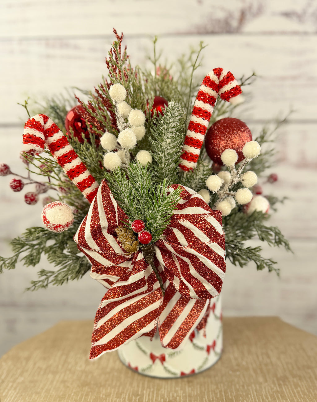 Handmade peppermint Christmas arrangement, white wall detail view of candy canes, striped bow and snowy greenery