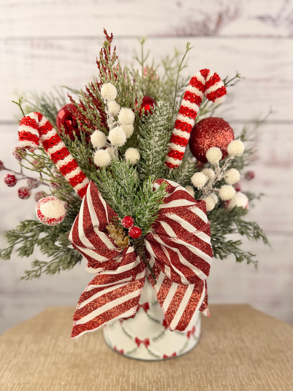 Handmade peppermint Christmas arrangement, white wall detail view of candy canes, striped bow and snowy greenery