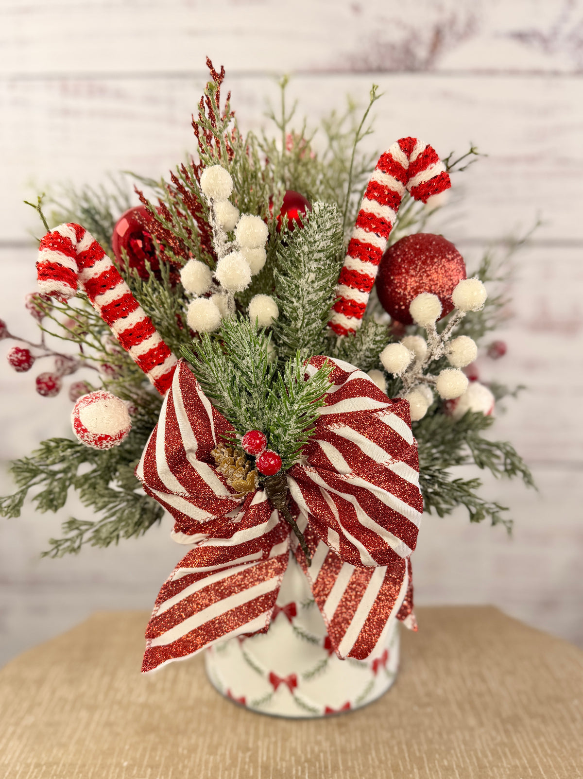 Handmade peppermint Christmas arrangement, white wall detail view of candy canes, striped bow and snowy greenery