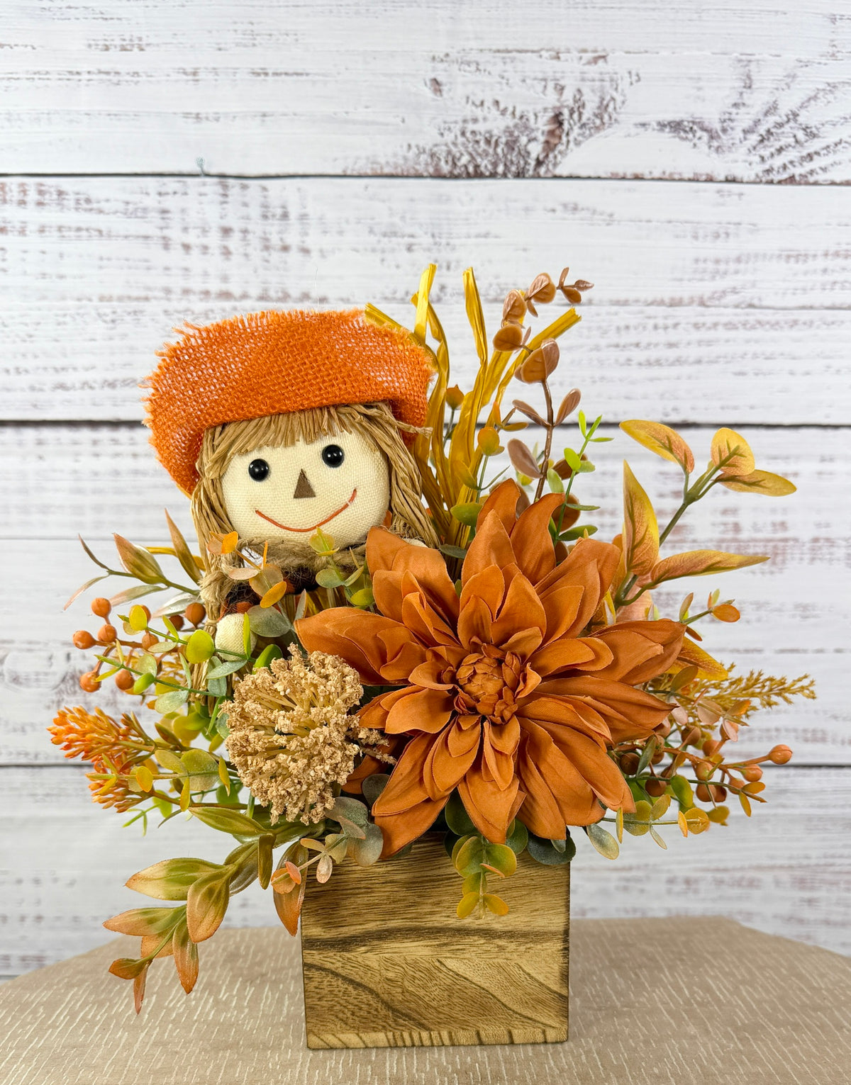 Sweet Scarecrow fall arrangement with smiling scarecrow, orange flowers and autumn foliage in a rustic wood cube box