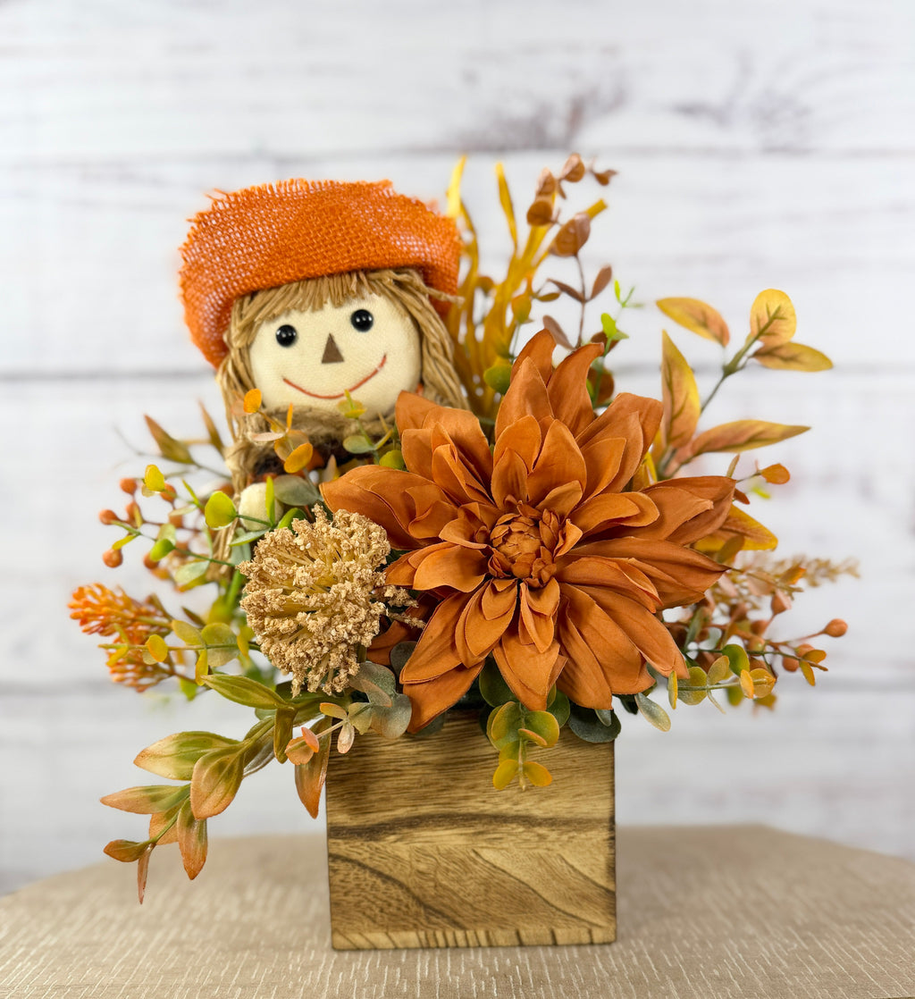 Sweet Scarecrow fall arrangement with smiling scarecrow, orange flowers and autumn foliage in a rustic wood cube box