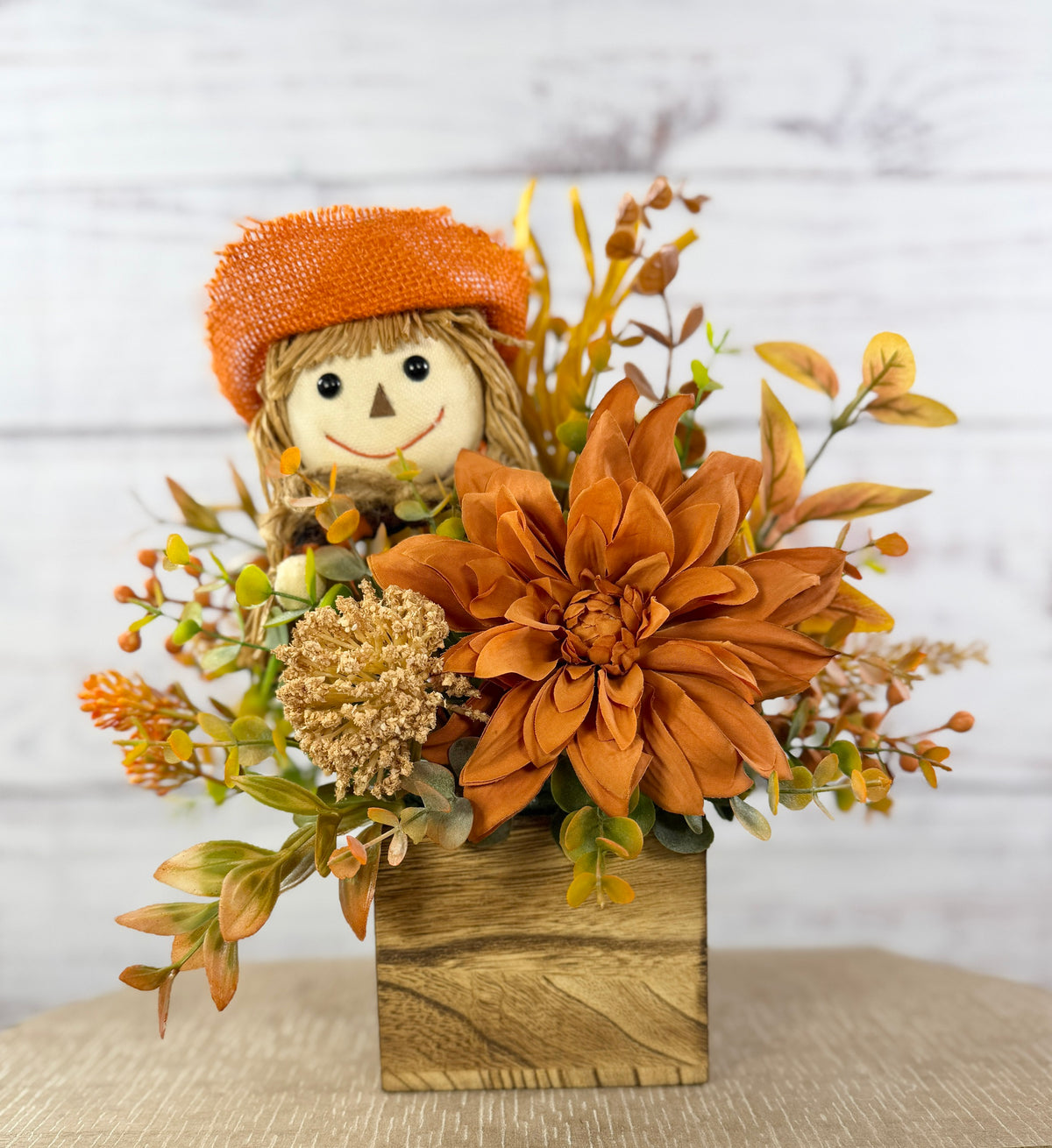 Sweet Scarecrow fall arrangement with smiling scarecrow, orange flowers and autumn foliage in a rustic wood cube box