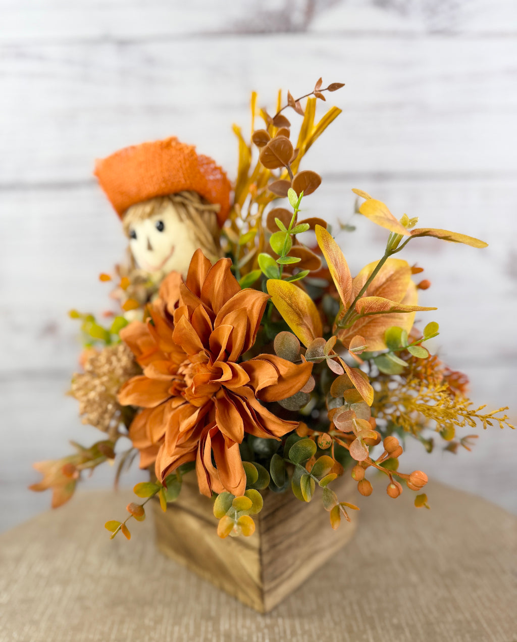 Sweet Scarecrow fall arrangement with smiling scarecrow, orange flowers and autumn foliage in a rustic wood cube box