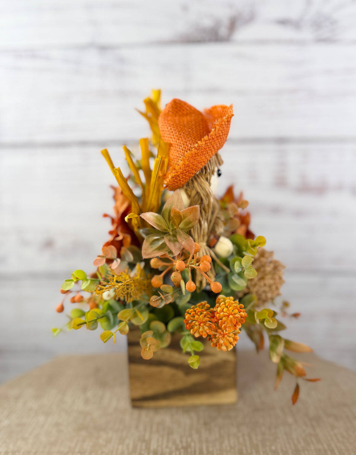 Sweet Scarecrow fall arrangement with smiling scarecrow, orange flowers and autumn foliage in a rustic wood cube box