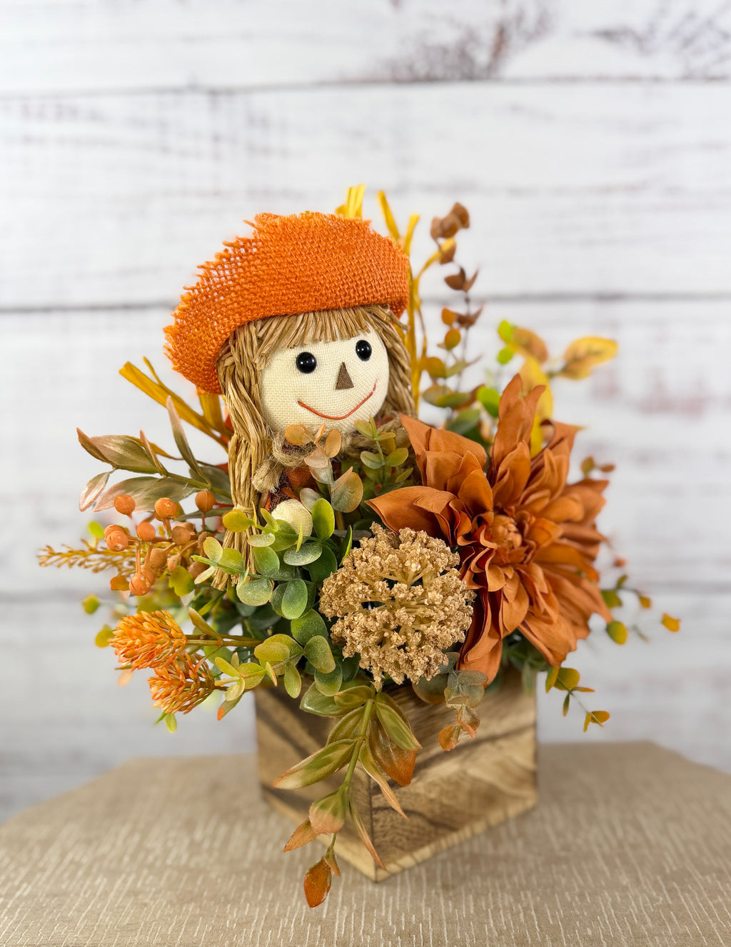 Sweet Scarecrow fall arrangement with smiling scarecrow, orange flowers and autumn foliage in a rustic wood cube box